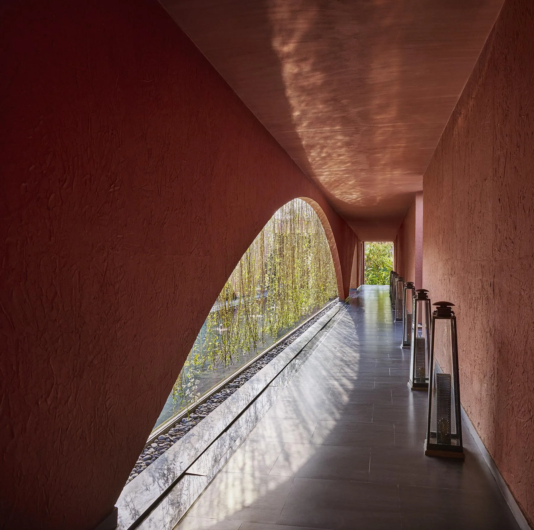 Shaded terracotta passage with a sweeping arch and hanging planting at Devasom