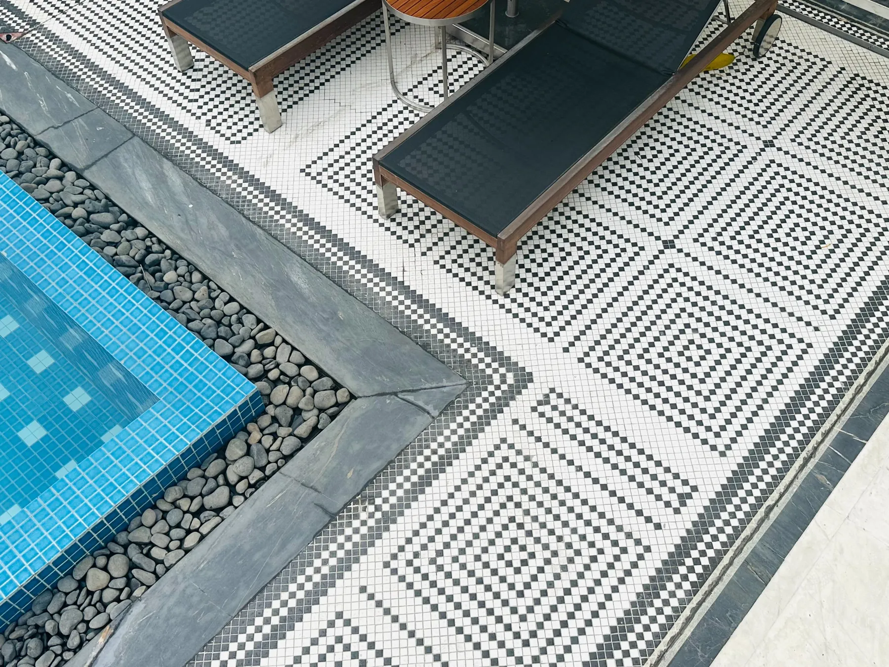 Blue pool edge, pebble band, patterned paving and a lounger at Devasom, Kolkata