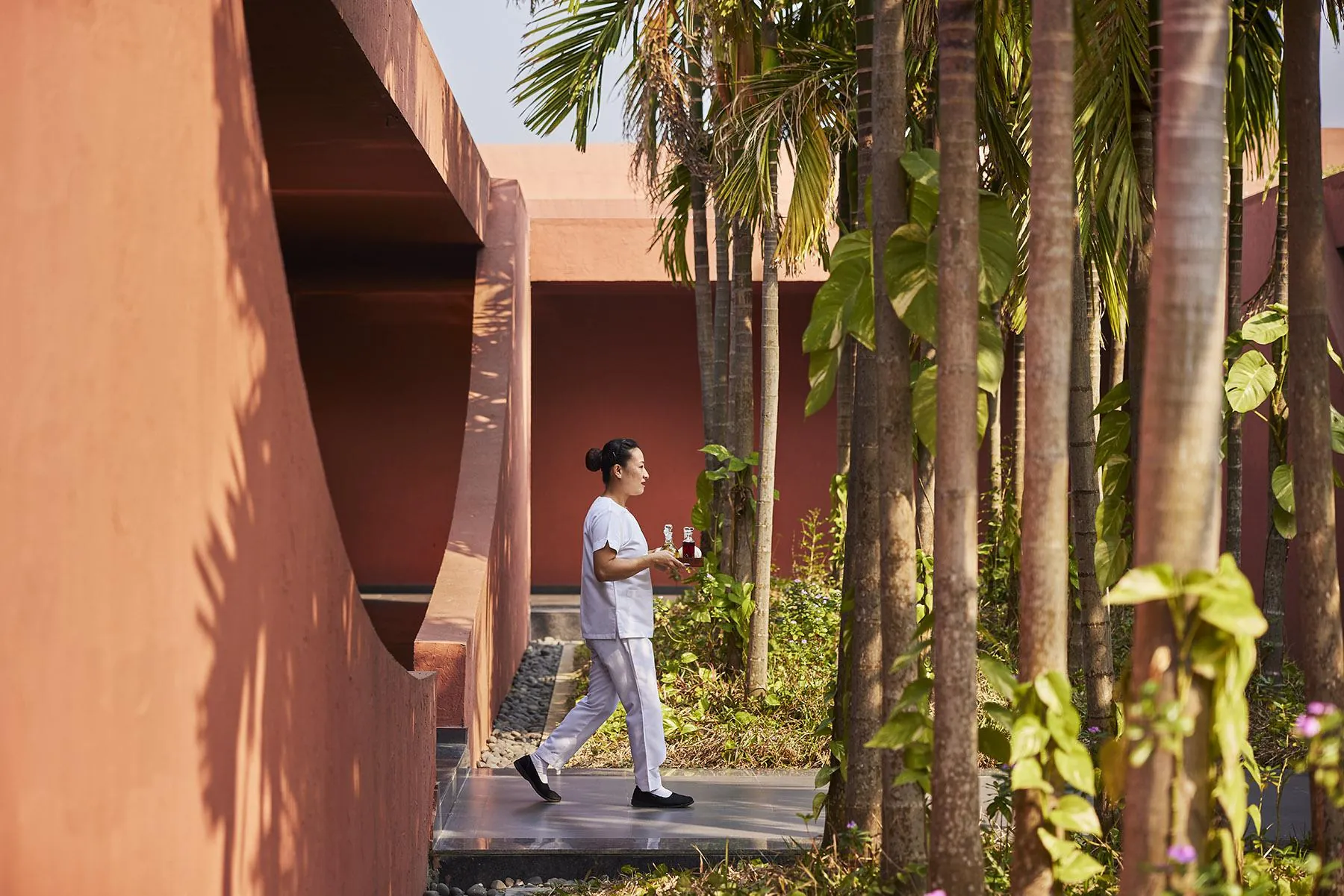 A visitor walking through a shaded palm courtyard at Devasom