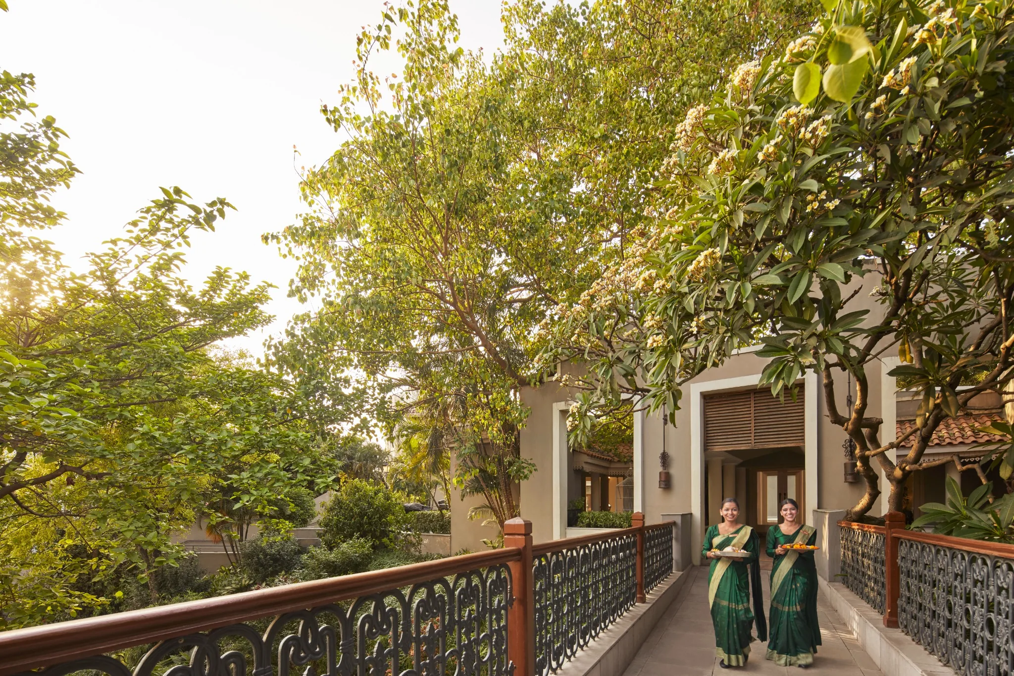 Arrival walkway with decorative railings beside mature trees at IHCL SeleQtions – Raajkutir, Kolkata